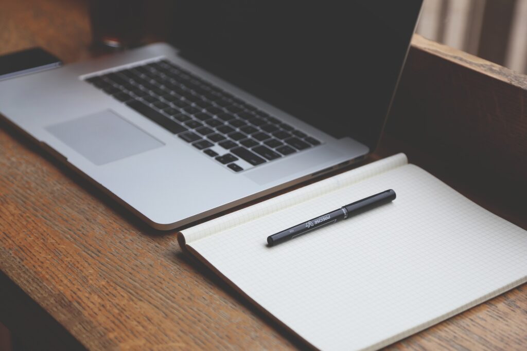 A laptop and a notebook with a pencil on a desk